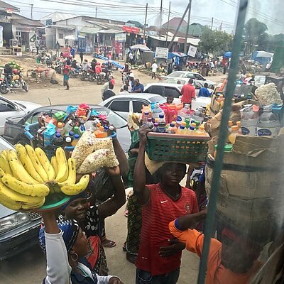 Straßenhändlerinnen und Händler tragen Körbe mit Obst und Waren auf dem Kopf durch eine belebte Marktstraße.