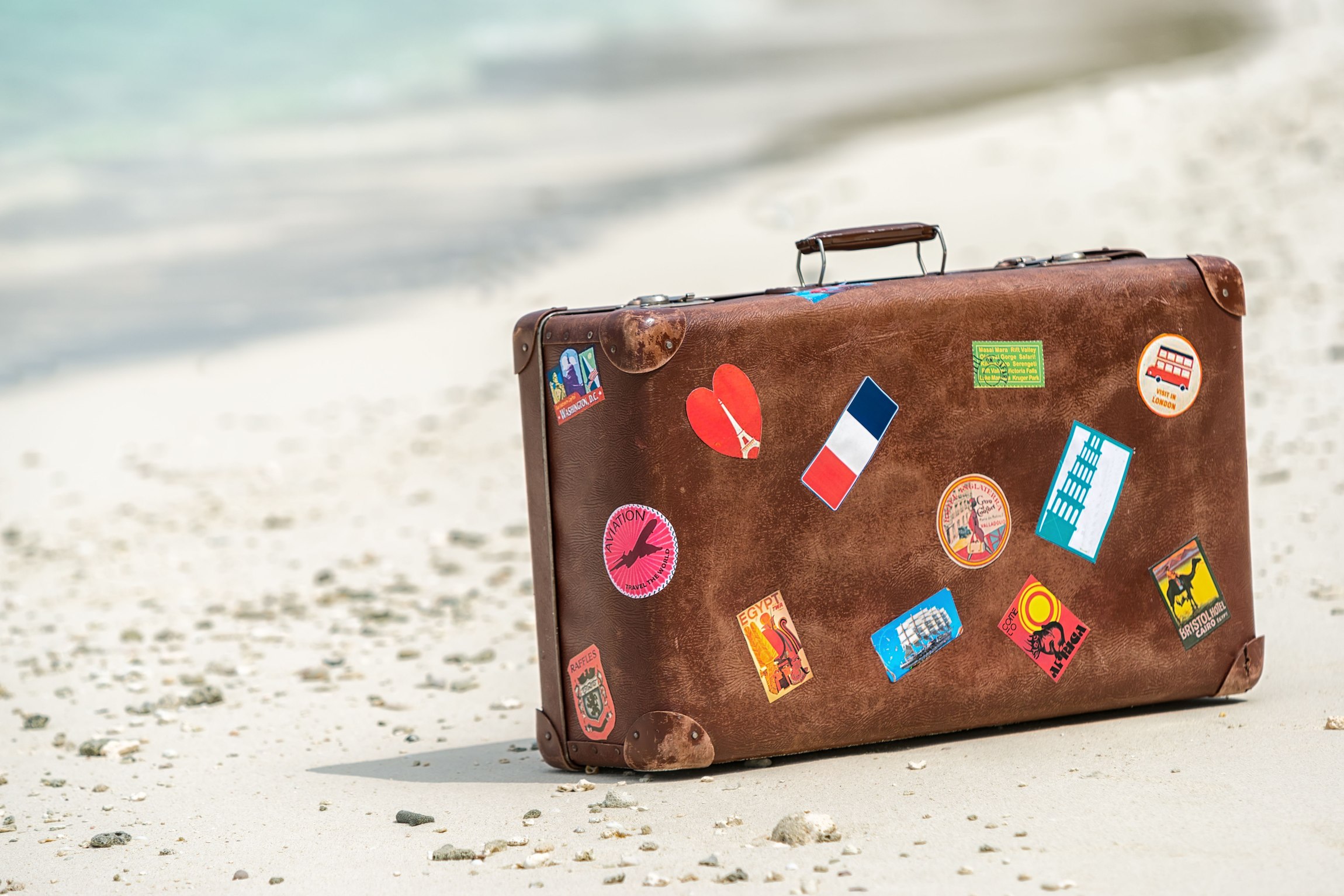Mit Stickern beklebter Koffer steht am Strand