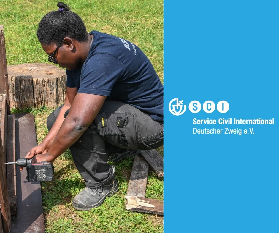 Person arbeitet mit einem Akkubohrer im Freien, daneben das Logo von Service Civil International.