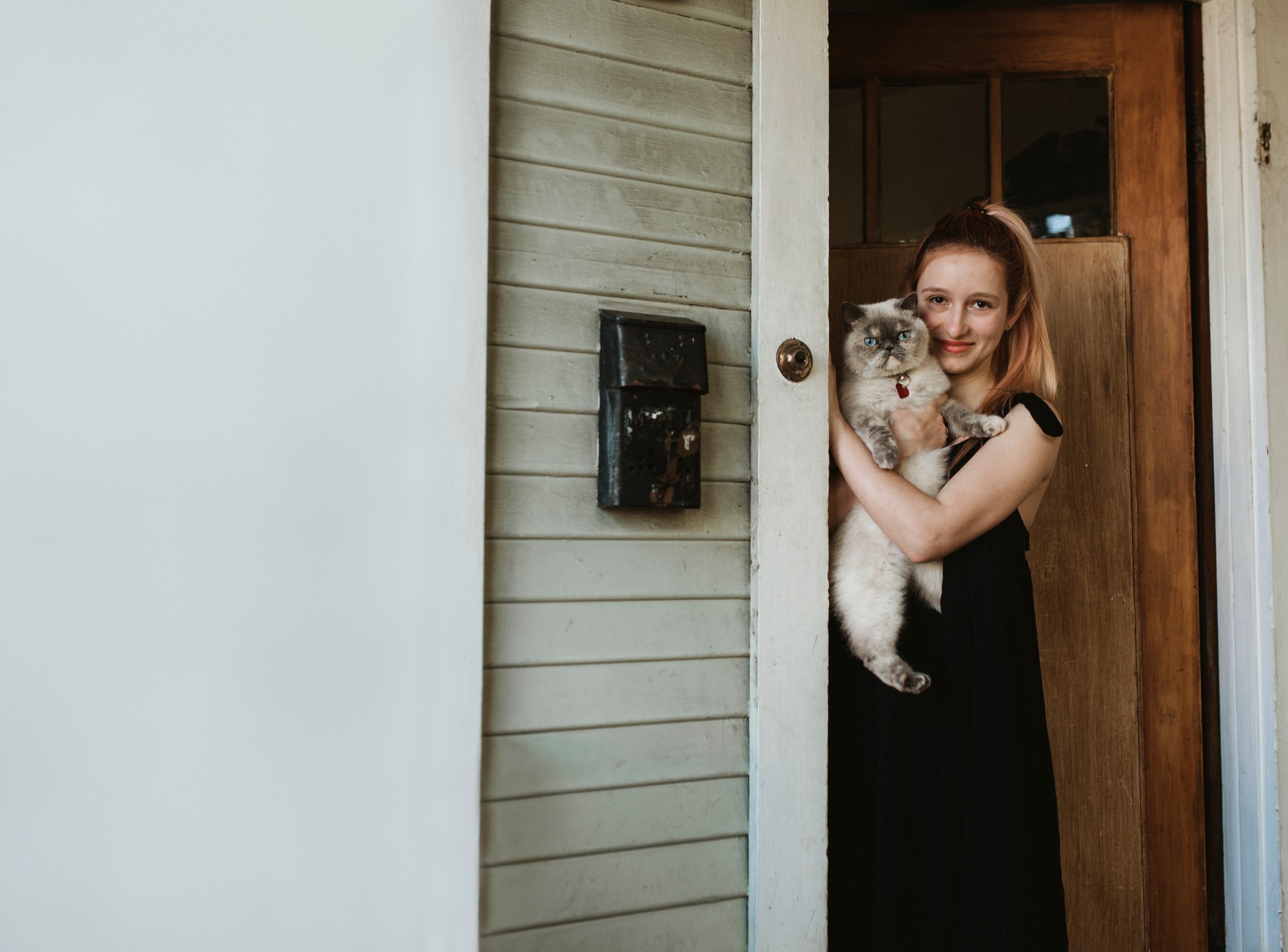 Junge Frau hat Katze auf dem Arm und steht in Haustür