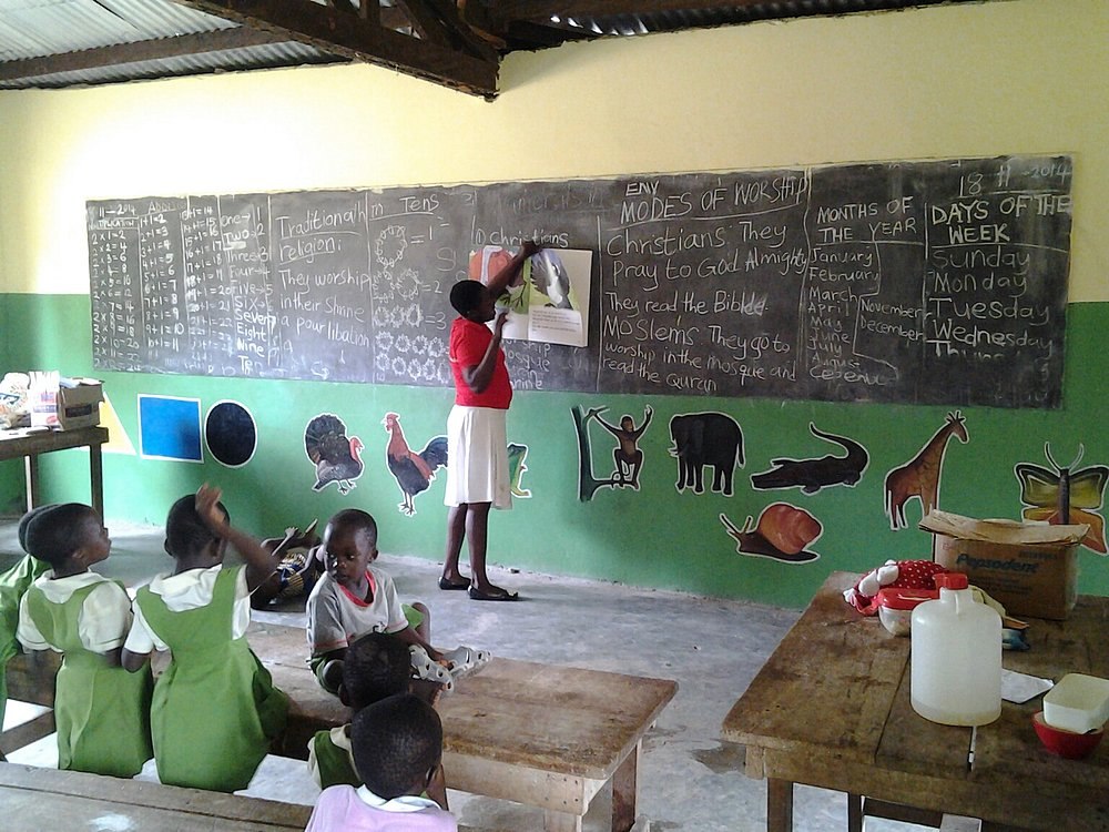 Kinder sitzen in einem Klassenzimmer in Ghana, während eine Person an der Tafel unterrichtet.