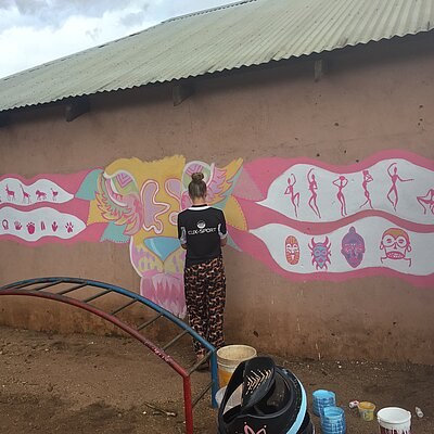 Eine Frau steht vor einer bemalten Wand mit bunten Mustern und Symbolen in Malawi.