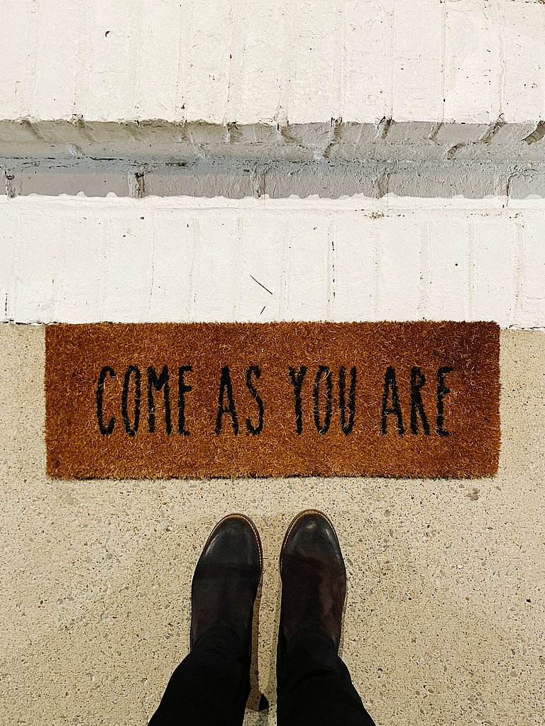 Füße stehen vor einer Fußmatte auf der "Come as your are" steht